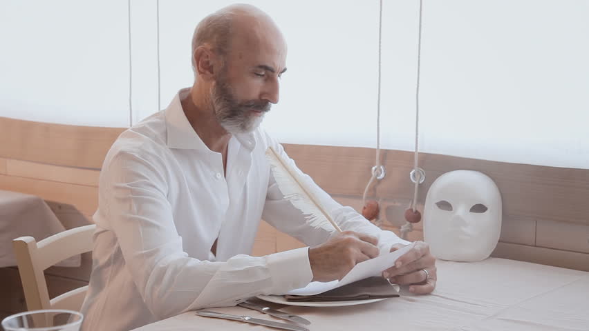 An old man writing a letter with a white quill pen near the soft light of a window. Front shot.
