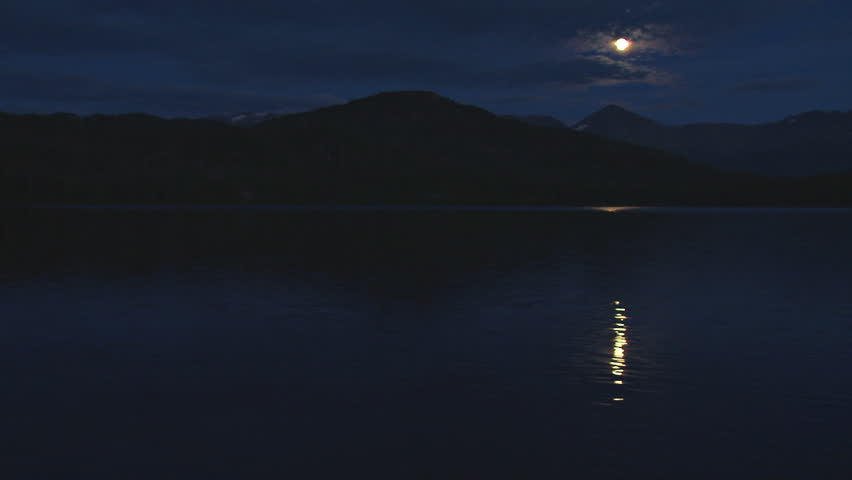 Moon beam reflected on dark lake waters, hill in the background. Moon reflection