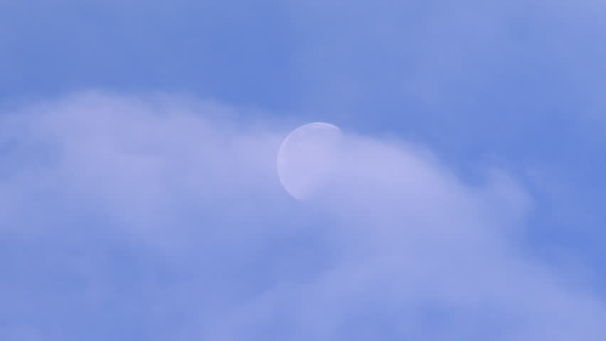 Waning gibbous moon revealed by passing clouds in a blue sky.