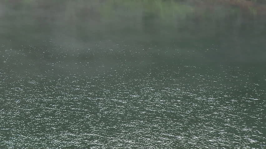 A light mist moves over the surface of a rippling lake with hazy green