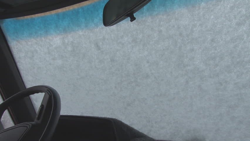 Windshield wipers scraping snow from windshield, shot from inside vehicle.