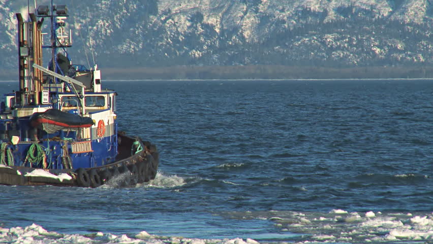 Pan/tracking shot of tugboat plowing through the icy waters as it leaves the