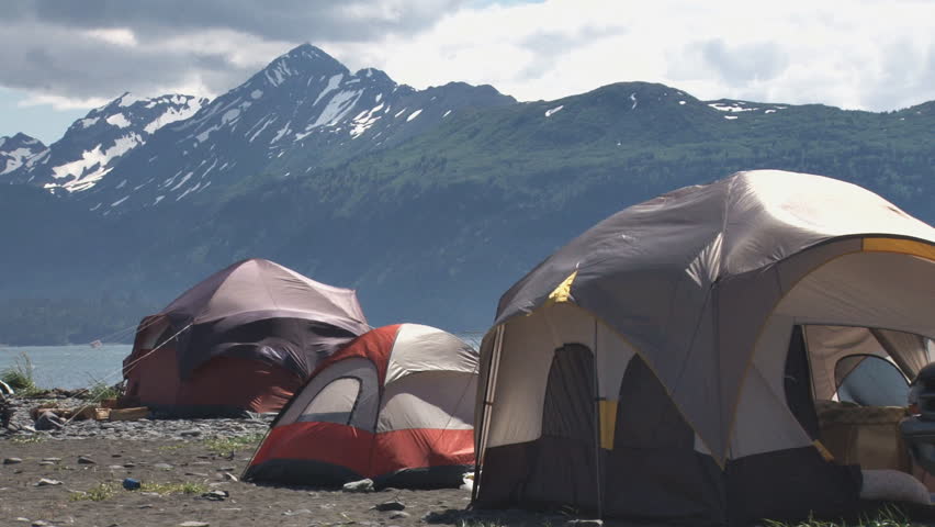 Tents billowing and flapping in a stiff breeze on the beach with mountains in