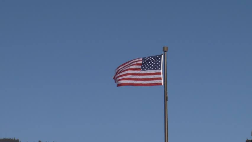 Zoom in to the American flag flying to the left in a moderate breeze in a clear