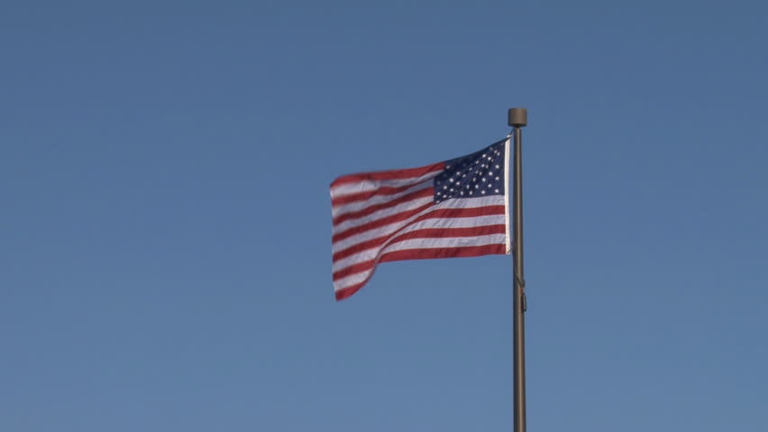 The American flag flies to the left in a moderate breeze in a clear sky.