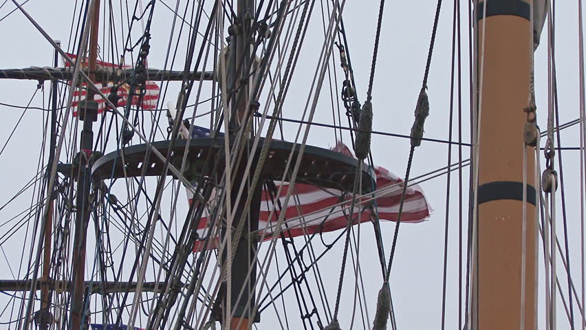 High in the rigging of a tall ship at harbor flies the Stars and Stripes, flag