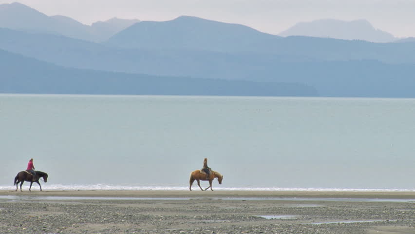 Two women on horses riding together on the beach.