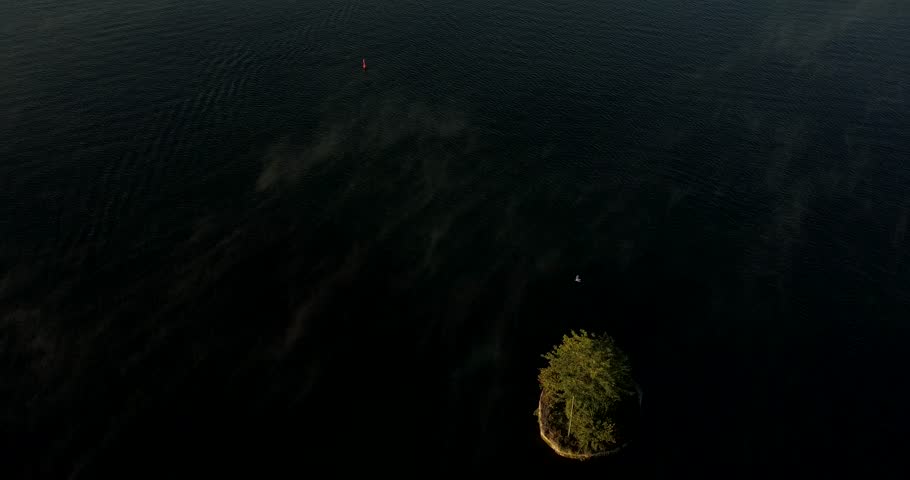 Drone orbits backwards to the left revealing a small island and a larger island with a cottage as mist rises and is blown across a lake.