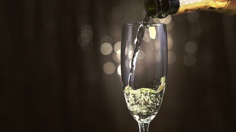 Champagne. One Flute with Sparkling Wine. Pouring Champagne over golden Holiday Bokeh Blinking Background. Celebrating. Glass of champagne close up. Slow motion 4K UHD video