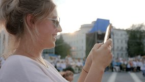 female in Sunglasses holds mobile phone standing at downtown, close-up,