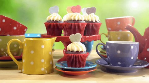 4k Colorful Mad Hatter style tea party with cupcakes and rainbow colored polka dot cups and saucers, with bokeh garden background and lens flare, static. 