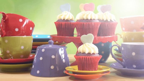 Colorful Mad Hatter style tea party with cupcakes and rainbow colored polka dot cups and saucers, with bokeh garden background and lens flare, panning across close up. 