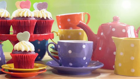 Colorful Mad Hatter style tea party with cupcakes and rainbow colored polka dot cups and saucers, with bokeh garden background and lens flare, panning up close up.  