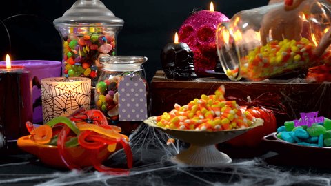 4k Happy Halloween trick or treat party table with bowls and apothecary jars of candy with skull candles against a black background, setting up table time lapse.