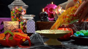 4k Happy Halloween trick or treat party table with bowls and apothecary jars of candy with skull candles against a black background, pouring candy close up. - Powered by Shutterstock - Get 15% off with code: PIKWIZARD15
