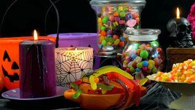 Happy Halloween trick or treat party table with bowls and apothecary jars of candy with skull candles against a black background, panning across and up. - Powered by Shutterstock - Get 15% off with code: PIKWIZARD15