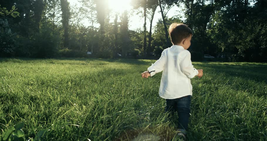 Cute baby boy with wite shirt running in grass field . Slow Motion. 4k. The camera behind the baby. Royalty-Free Stock Footage #31198906