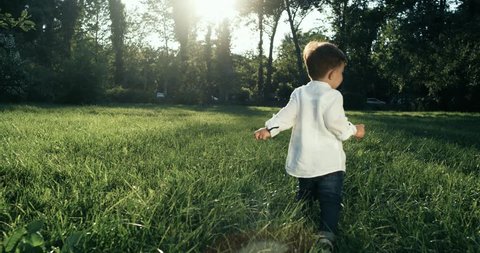 Cute baby boy with wite shirt running in grass field . Slow Motion. 4k. The camera behind the baby.