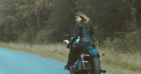 TRACKING female biker riding her motorcycle on a forest road