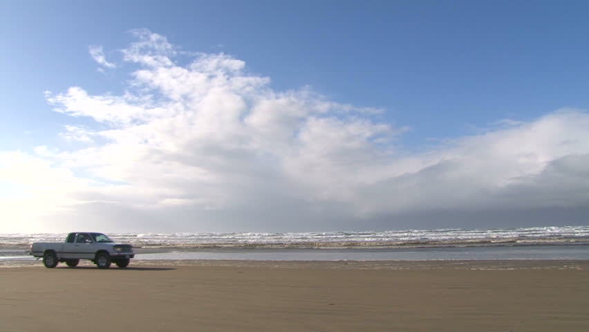Pickup truck on Pacific sandy beach drives through frame.