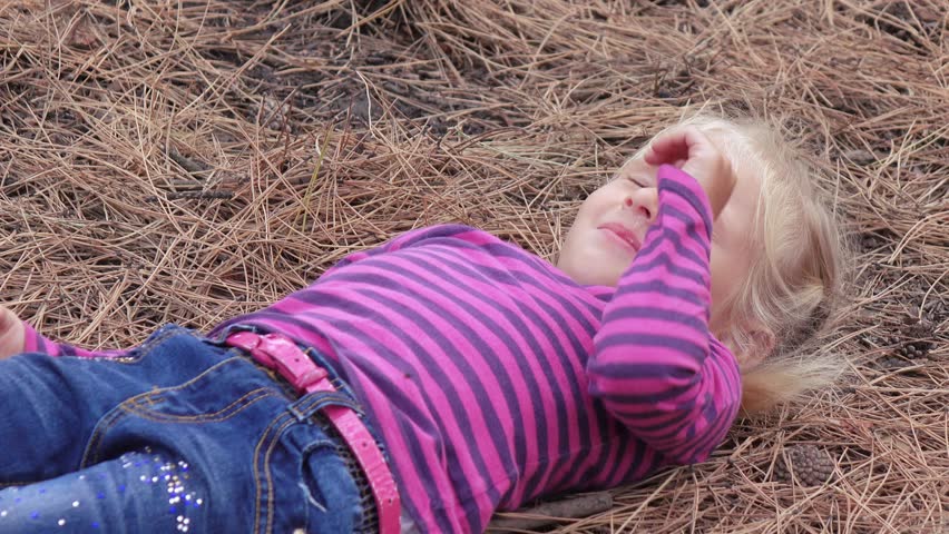On the pine needles the little girl the child looks at the sky and squintes