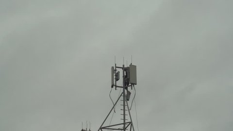 The technician serves the antennas of mobile telephony, internet, television on the background of the gray sky. The electronics engineer is dismantling the cellular aerial.