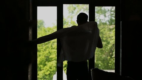 Man putting on shirt standing by window at home, slow motion