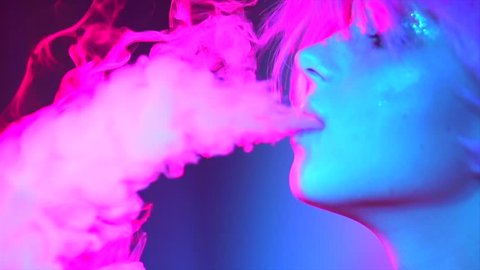 Fashion art portrait of beauty model woman in bright lights with colorful smoke. Smoking girl, Close up of a female inhaling from an electronic cigarette. Night life concept. 4K UHD Slow motion video