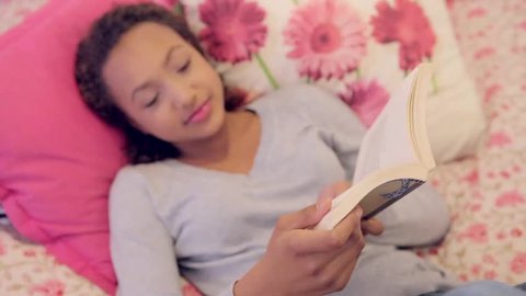 Portrait of a young teenage girl reading a book while laying down on a bed at home. Focus on hands. Stock video