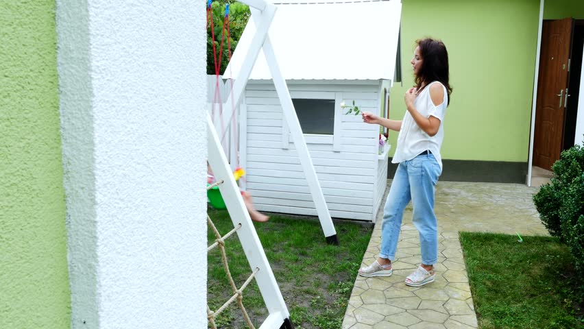 summer, in the garden, mother, beautiful young woman, swinging on a swing her one-year-old daughter. The family spends their leisure time together.