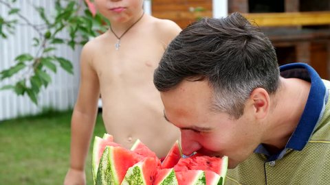 in summer, in the garden, father with a four-year-old son cut a watermelon and eat it, have fun, a boy likes watermelon very much. sweet watermelon for lunch with family.