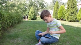 the boy is playing on the tablet on the grass
