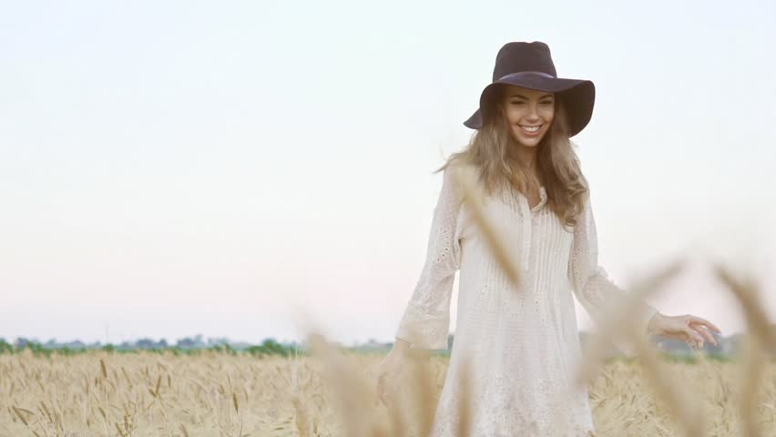 Happy young pretty woman in white dress and black hat running in the field