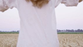 Back view of young happy woman in white dress and black hat running in the field