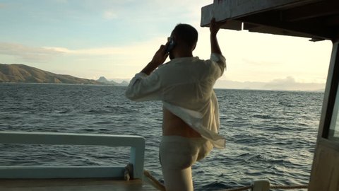 Handsome man standing on the luxury yacht and chatting on cellphone, slow motion shot at 240fps, steadycam shot 
