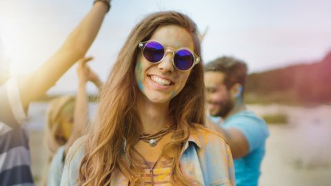 Close-up Portrait of a Beautiful Young Girl with Sunglasses Standing in the Crowd of People Celebrating Holi Festival. People Throwing Colorful Powder in Her Back.  Shot on RED EPIC-W 8K Helium Camera