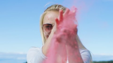 Beautiful Young Blonde Blows Holi Colorful Powder Off Her Hands and Laughs. Clear Blue Sky Behind Her. Shot on RED EPIC-W 8K Helium Cinema Camera.