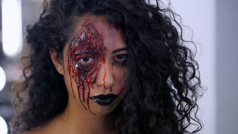 Scary portrait of young girl with Halloween blood makeup. Beautiful latin woman with curly hair looking into camera. Slow motion.