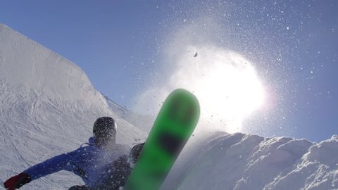 SLOW MOTION: Young pro snowboarder riding the half pipe in big mountain snow park, performing spraying trick over the sun on halfpipe wall in sunny winter
