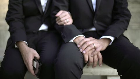 Great slow motion of a couple of a homosexual gay couple of men in black suit with wedding rings and a smartphone in the hand.