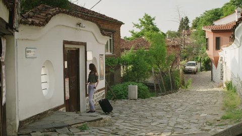 Wide slow motion shot of woman with suitcase knocking on door of house / Plovdiv, Bulgaria