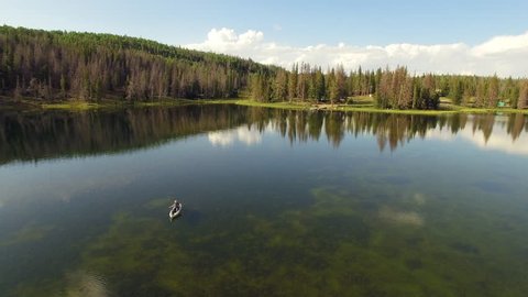 Aerial view rotating around woman fishing in kayak in glassy lake.
