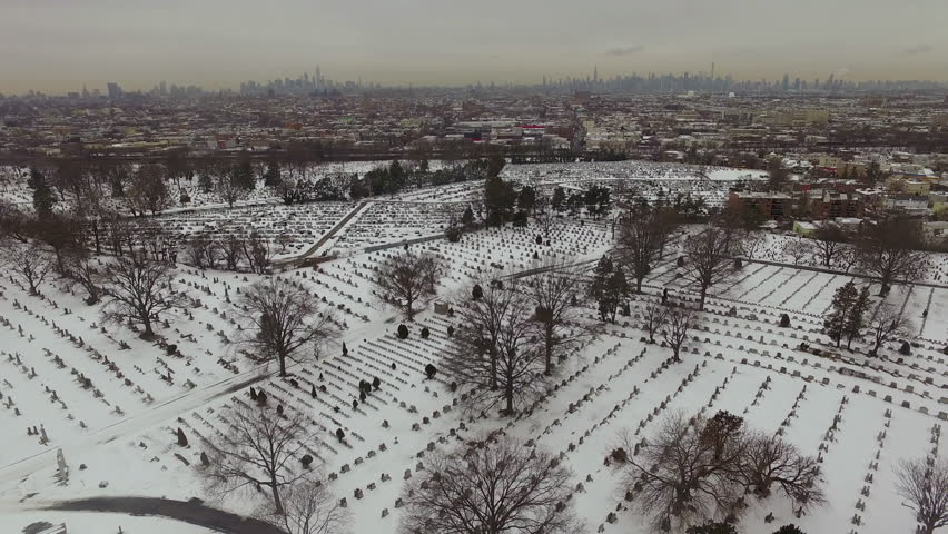 Aerial shot of snowy graveyard with city skyline in the background.