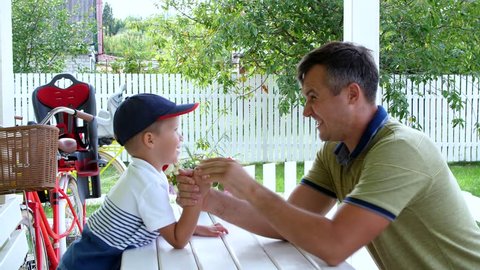 Dad and his four-year-old son play together in armwrestling, they are having fun. In the summer, in the garden.
