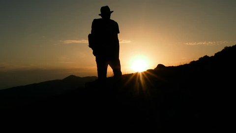 Male Mountain Climber In Summer. Man Hiking in Mountains Enjoying Success. Hiking Walking Slow Motion Recreation Activity. Holiday Vacation Tourism, Outdoors Man Hiking Silhouette  Beautiful Sunset.