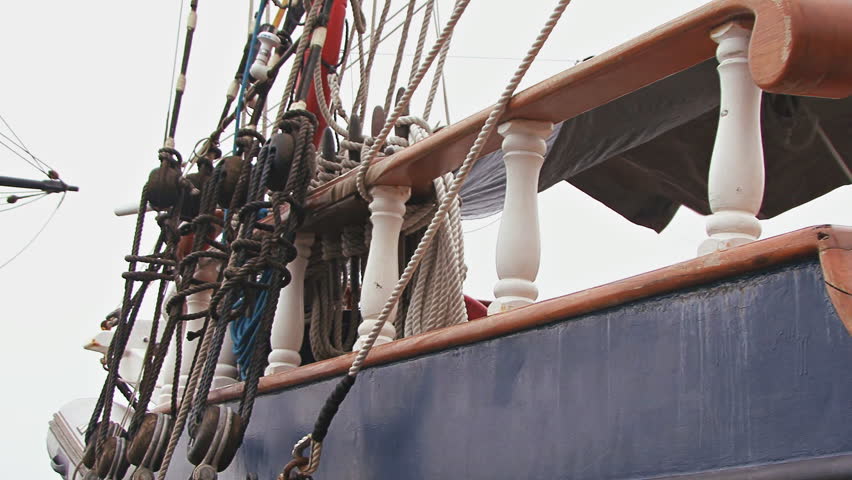 Pan right past railing to the helm of a contemporary square-rigger at harbor.