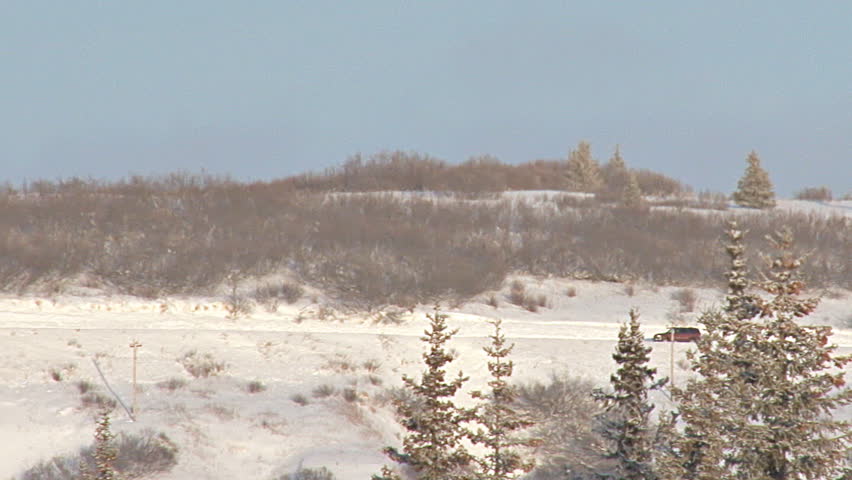 Long shot of SUV driving left to right on snowy road in Alaska.