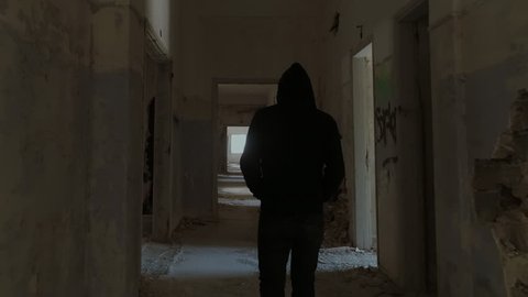 Hooded young man inside destroyed abandoned building,slow motion,dramatic.A sad young man facing social issues, walking inside a big wrecked empty building in slow motion.Drone/dolly motion.