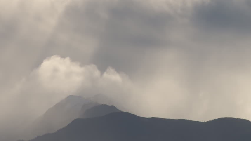 Heavy clouds interspersed with glowing rays of sunlight over a mountain ridge