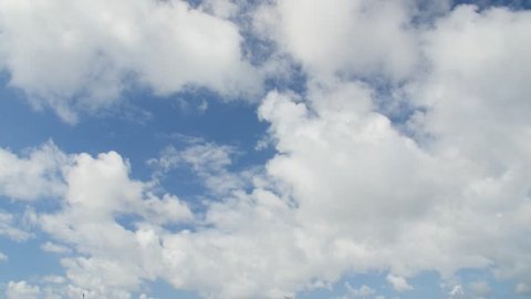 Time lapse clip of fast moving white fluffy clouds over blue sky.